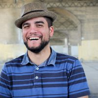 Carlos Centeno smiling as he wears is tan-colored fedora.